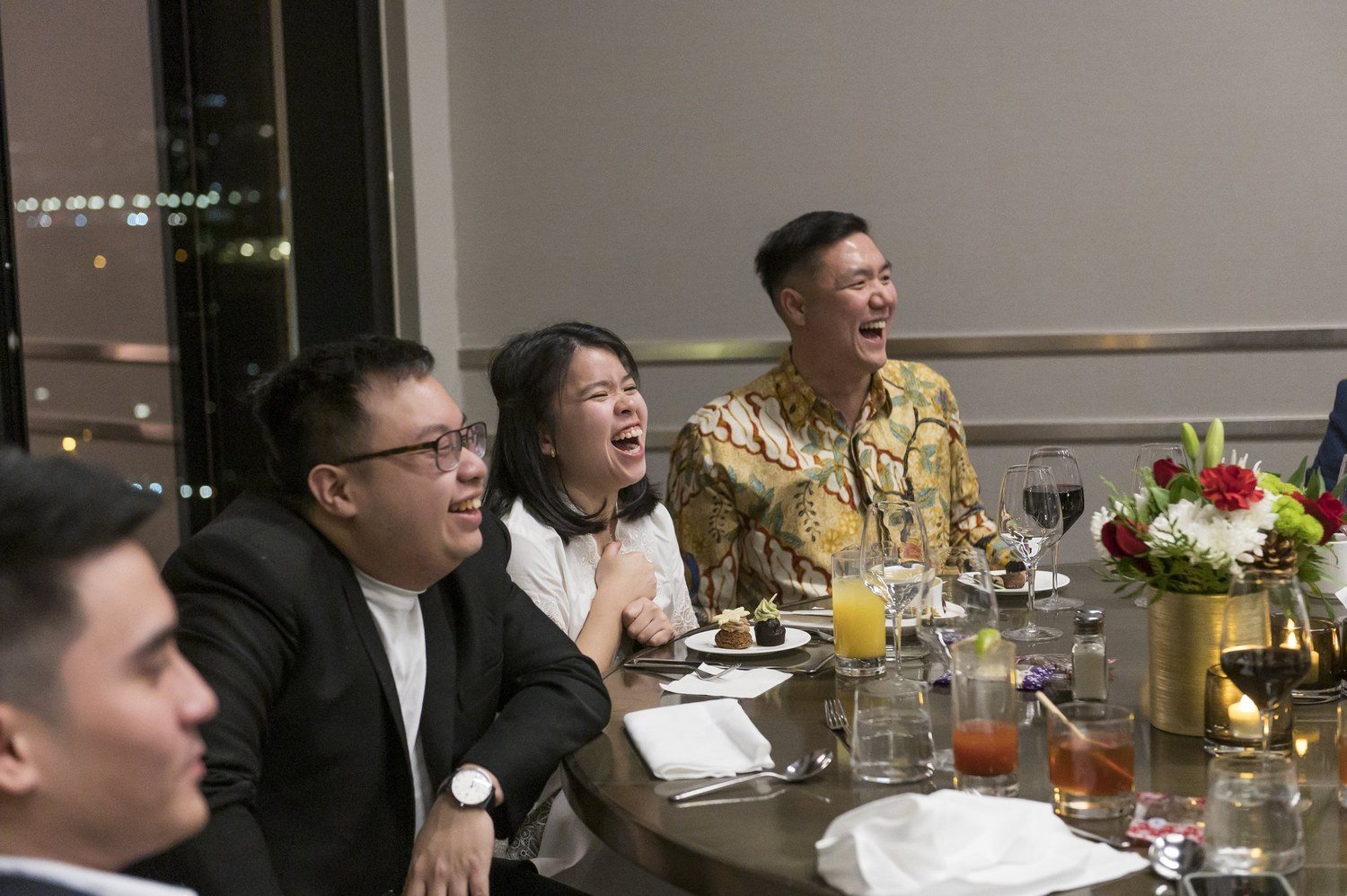 John Ha entertaining a lively dinner table as guests laugh during a Vancouver event